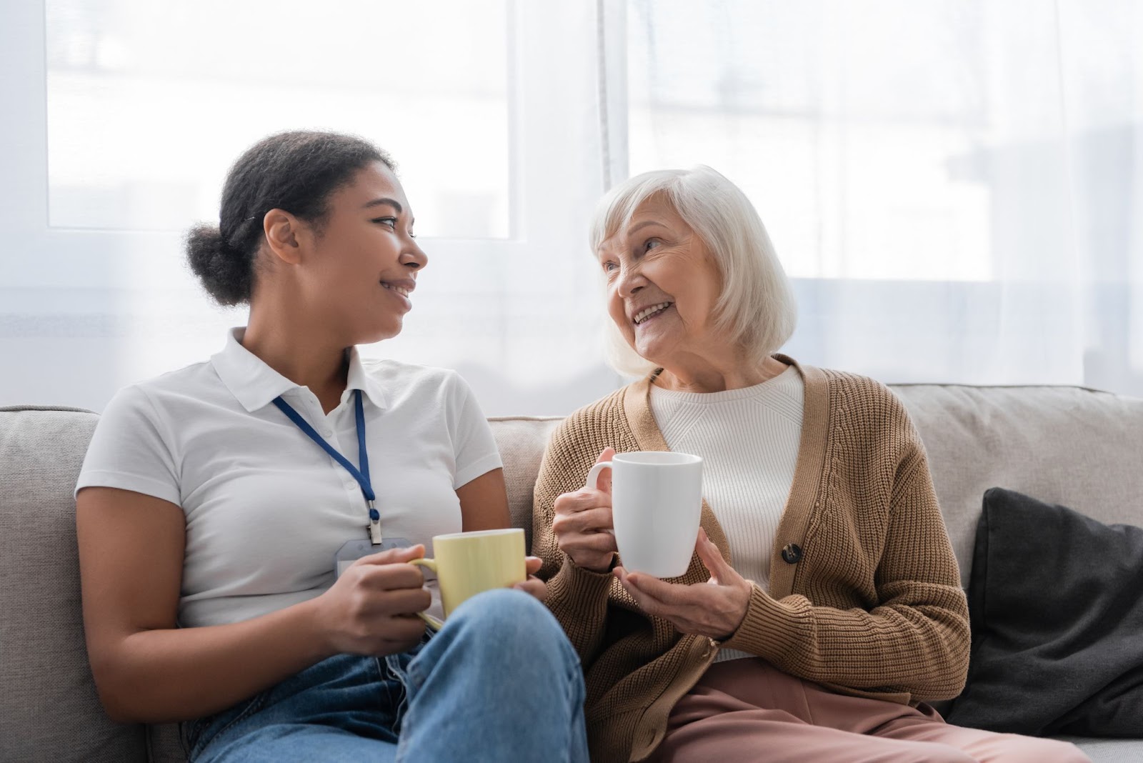 A senior support worker enjoys a cup of tea with a smiling senior.
