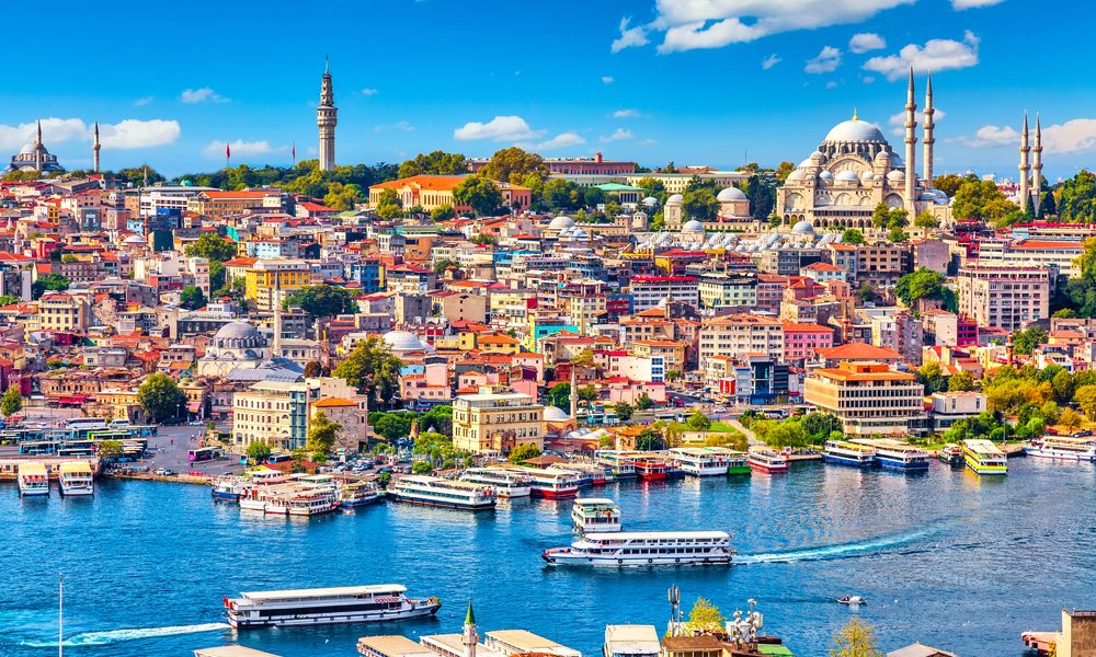 Colorful cityscape of Istanbul with historic mosques, vibrant buildings, and boats sailing on the Bosphorus under a bright blue sky.