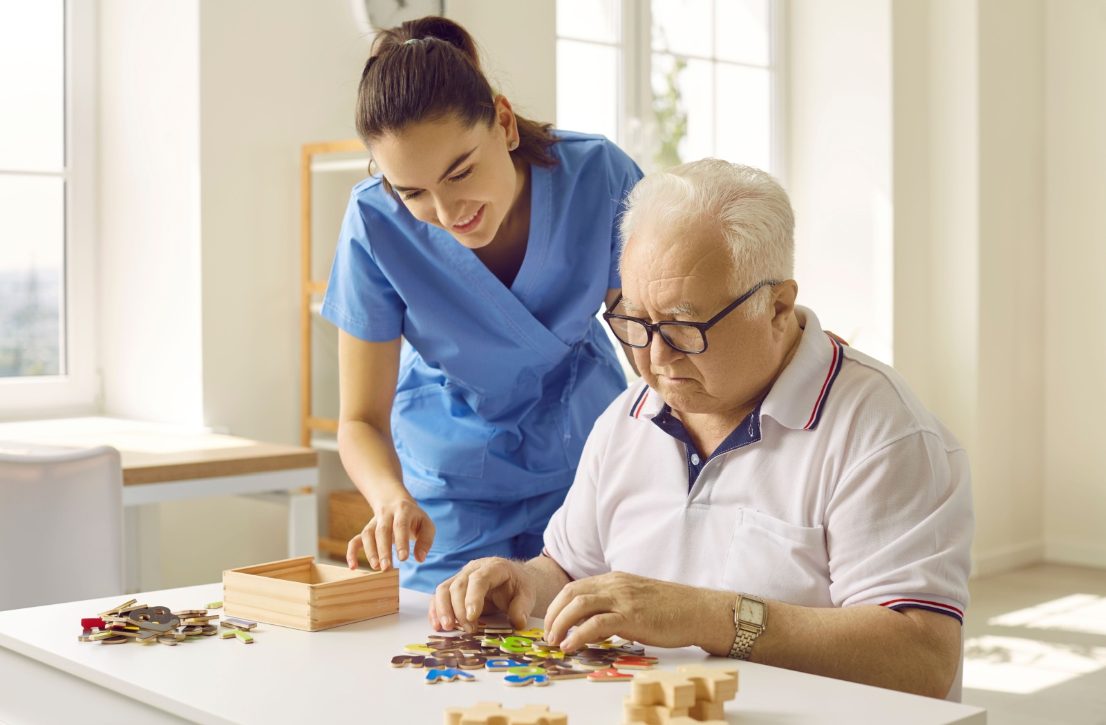 A caregiver assisting an older adult with a puzzle in a memory care setting.