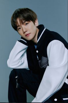 This contains an image of EXO Baekhyun sitting on top of a chair wearing a black and white sweater jacket