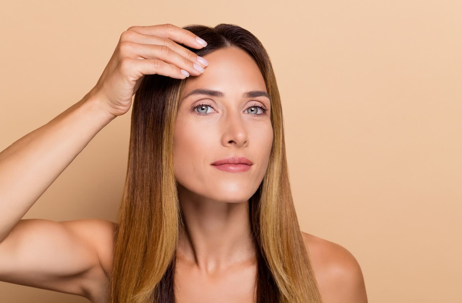 A patient uses their hand to part their hair and look at the results of their Botox treatment
