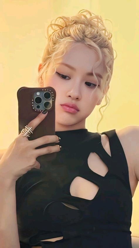 This contain Rosé holding a cell phone in her right hand and wearing a black dress with cutouts on it