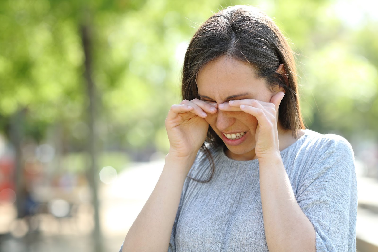 A woman spending time outdoors rubs her irritated eyes.