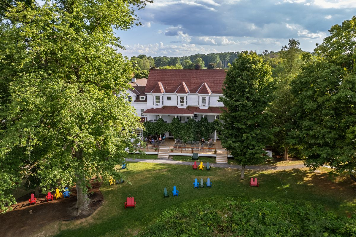 Lawn in front of Basin Harbor main building with green trees and multi-colored Adirondack chairs 