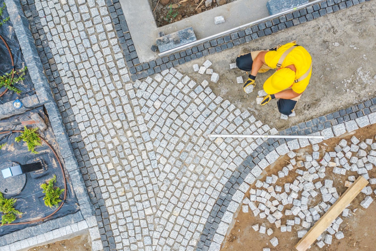 A construction worker in yellow gear carefully lays patterned natural stone pavers to create a curved pathway.