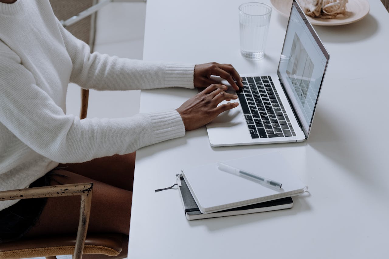 A person is typing on a laptop placed on a white desk. 