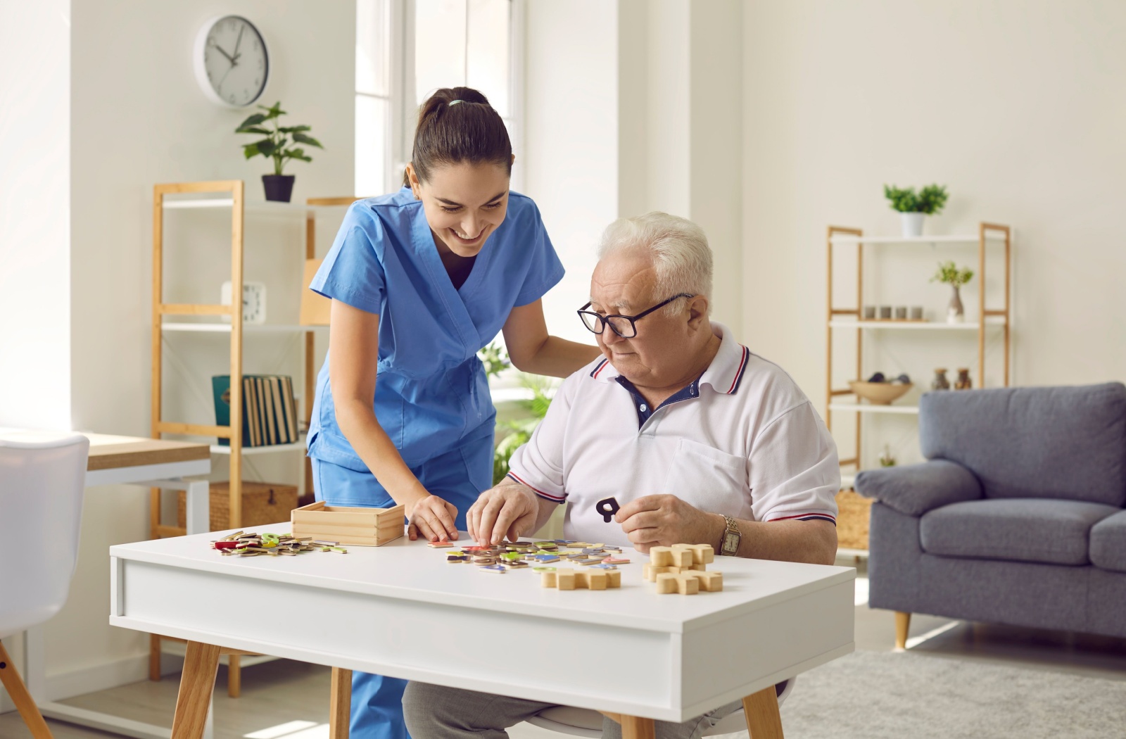 A caregiver and an older man with dementia smiling while working on a jigsaw puzzle after a move to memory care.