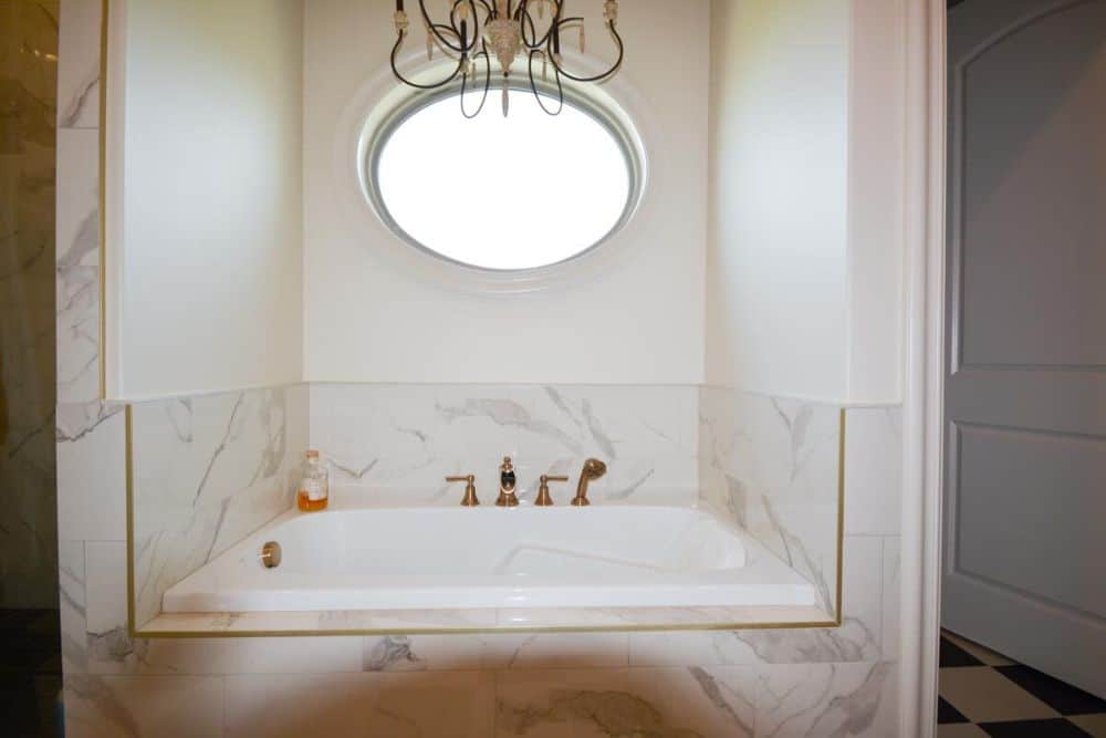 Deep soaking tub with marble backsplash and copper fixtures.