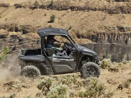 A black 2025 Yamaha Wolverine X2 riding through a brush-covered trail, featuring one driver and one passenger. 