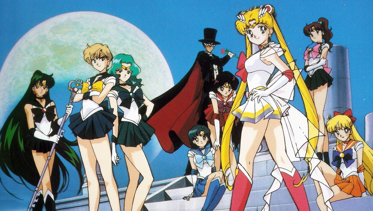 Personajes de Sailor Moon, incluidas Sailor Moon, Sailor Mercury, Sailor Mars, Sailor Jupiter, Sailor Venus y Tuxedo Mask, posando bajo la luz de la luna en un escenario urbano.