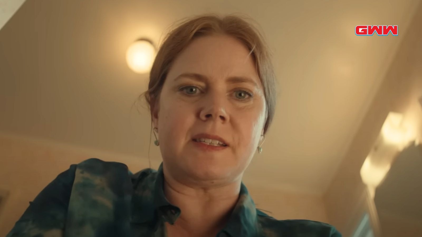 Amy Adams looking downward, appearing pensive in a warmly lit room.