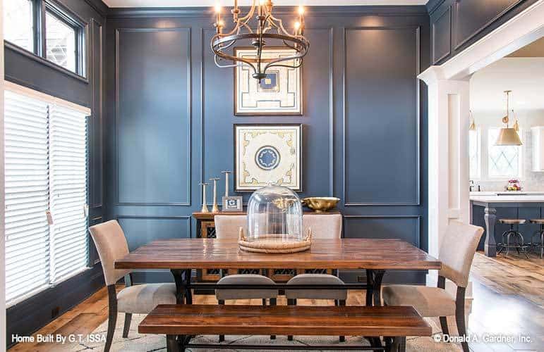 Formal dining room with blue wainscoted walls, a wooden buffet, and a rectangular dininng set well-lit by a wrought iron chandelier.
