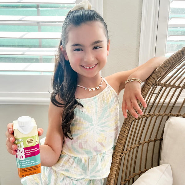 A young girl seated in a chair, cheerfully holding a juice bottle.