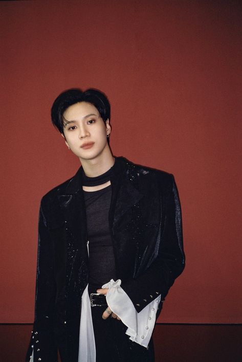 This containTaemin standing in front of a red wall wearing a black jacket and white scarf