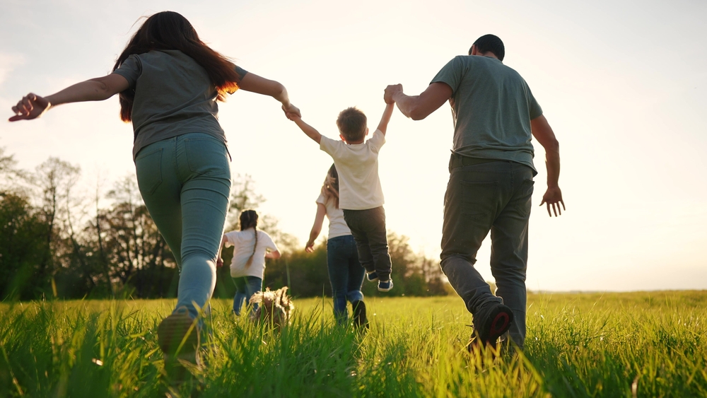 A family runs through tall grass together at sunset.