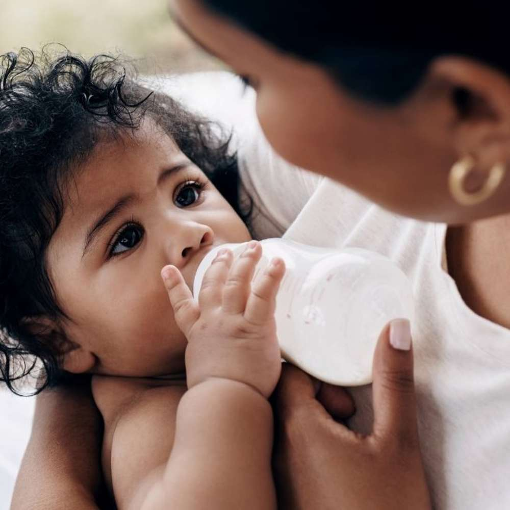 A mother is feeding her infant with a bottle, highlighting a tender bonding experience.
