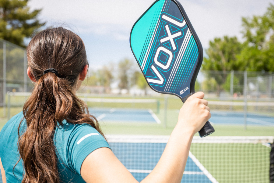 Pickleball player getting ready to serve with a Voxl paddle and pickleball on an outdoor court.