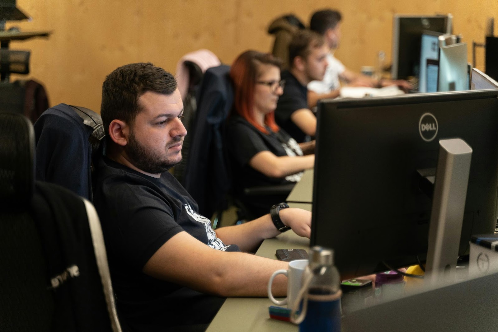 a person sitting at a desk with a computer and other people in the background