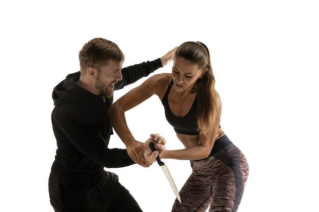 Man in black outfit and athletic caucasian woman fighting on white studio background. Women's self-defense, rights, equality concept. Confronting domestic violence or robbery on the street.