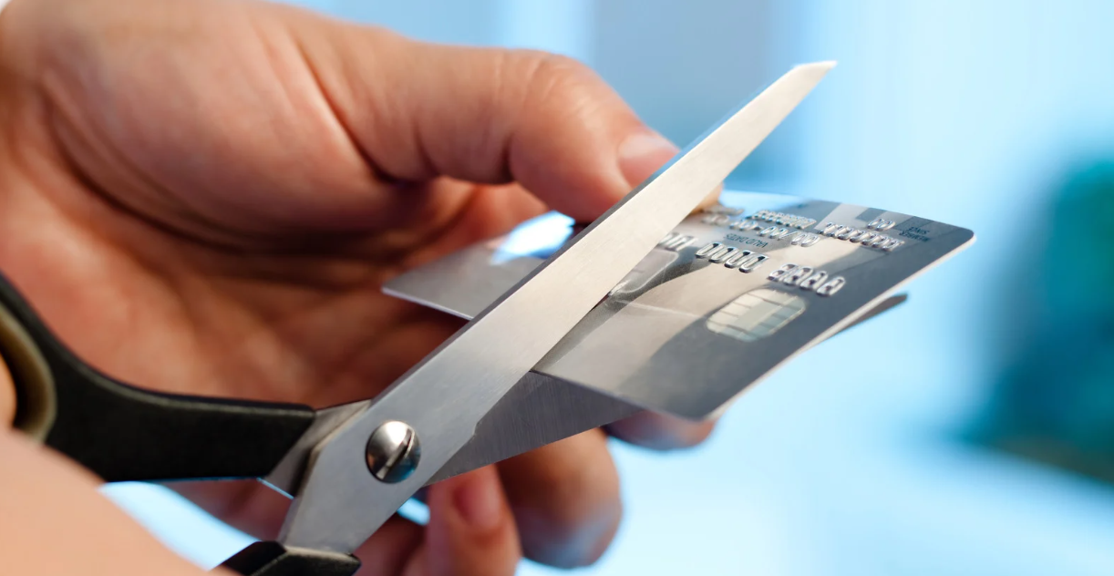 (Close-up of a hand cutting a credit card with scissors, symbolizing taking control of debt and breaking free from high-interest financial burdens.)