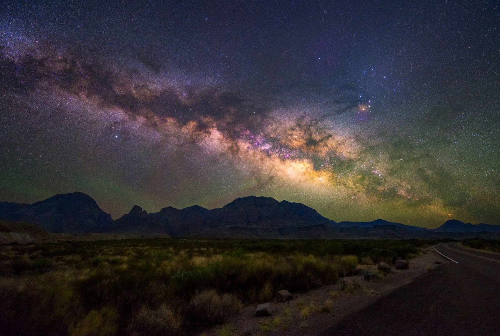 The Milky Way visible over a small mountain range, an empty grassy field in the foreground inside Big Bend National Park