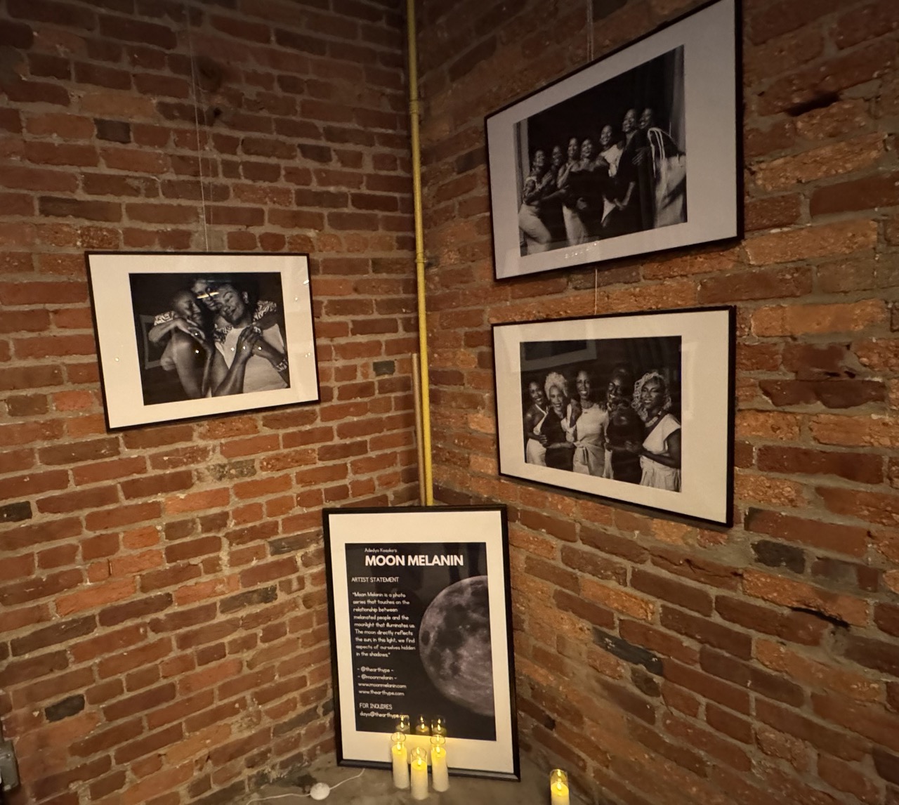 Black and white photos of women are hung on a brick wall.