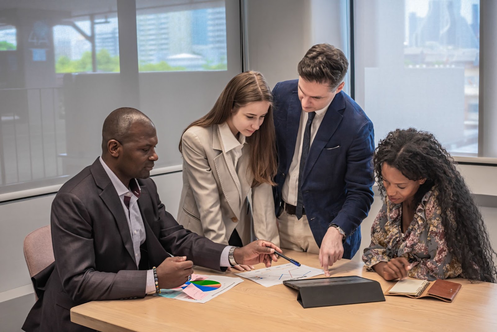 Business professionals review a project on a tablet with a financial consultant alongside a pie chart and graph on the table.