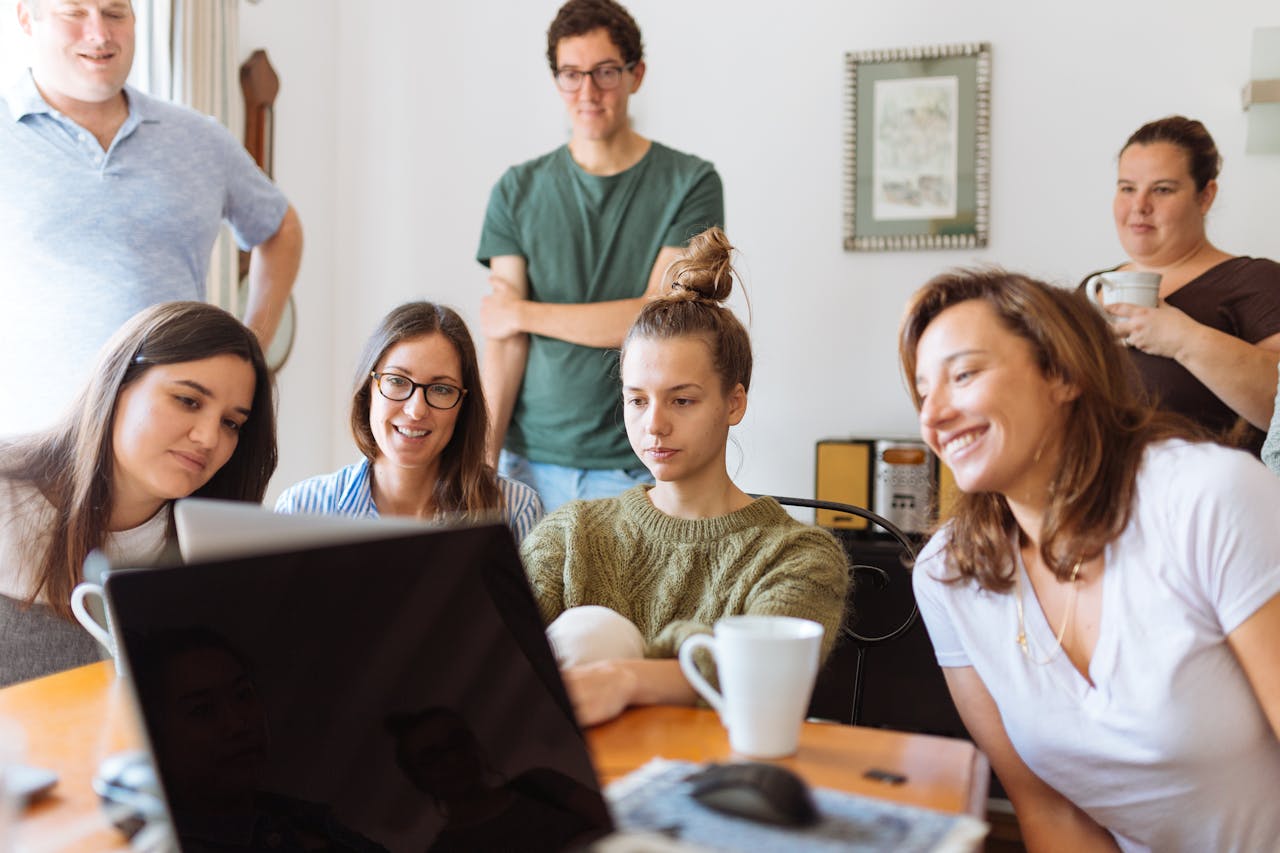 Group of colleagues gathered around a laptop, collaborating in a casual setting to manage small business projects and ideas