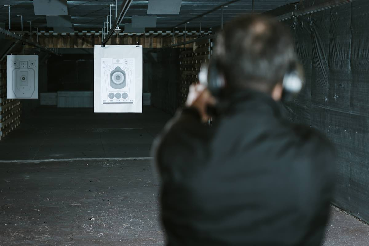 backshot of a man in a black shirt aiming at a target with a handgun