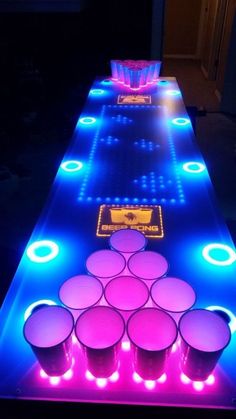 This contain an  image of illuminated table with cups on it and neon lights at the top, along with plastic cups lined up in rows