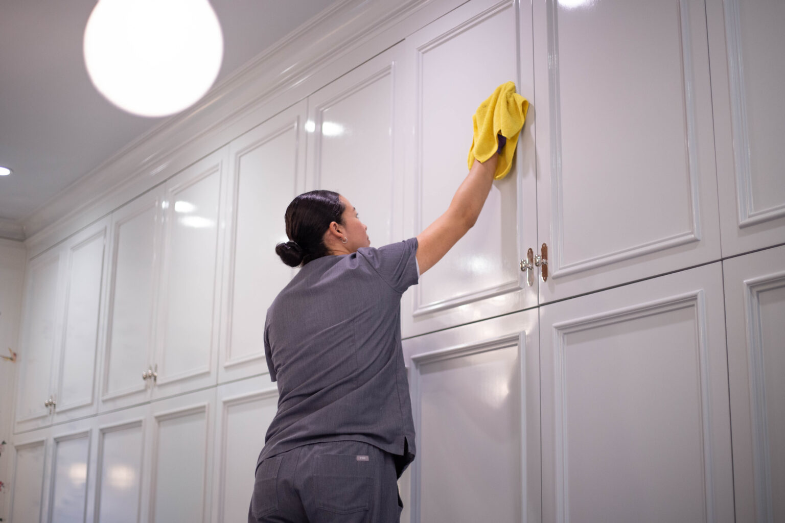 A cleaning staff from Vella’s deep clean service wiping down the cupboards with an eco-friendly cleaning solution on a microfibre cloth. 