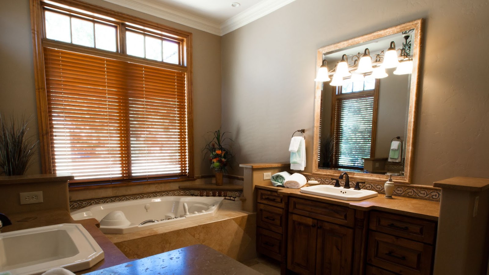 A luxurious, compact bathroom with a porcelain bathtub and sink, wooden cabinets, and glass windows adorned with brown blinds that complement the color scheme.