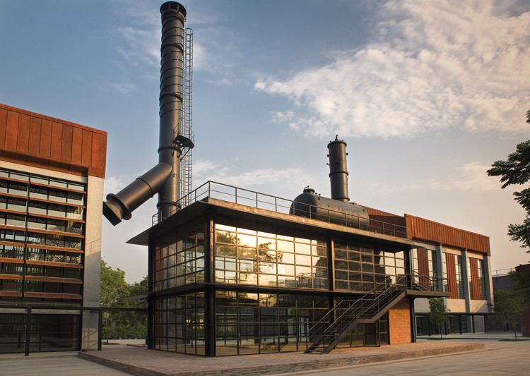 An industrial building with large metal chimneys and a modern glass facade reflecting the sky showcases sustainable development.