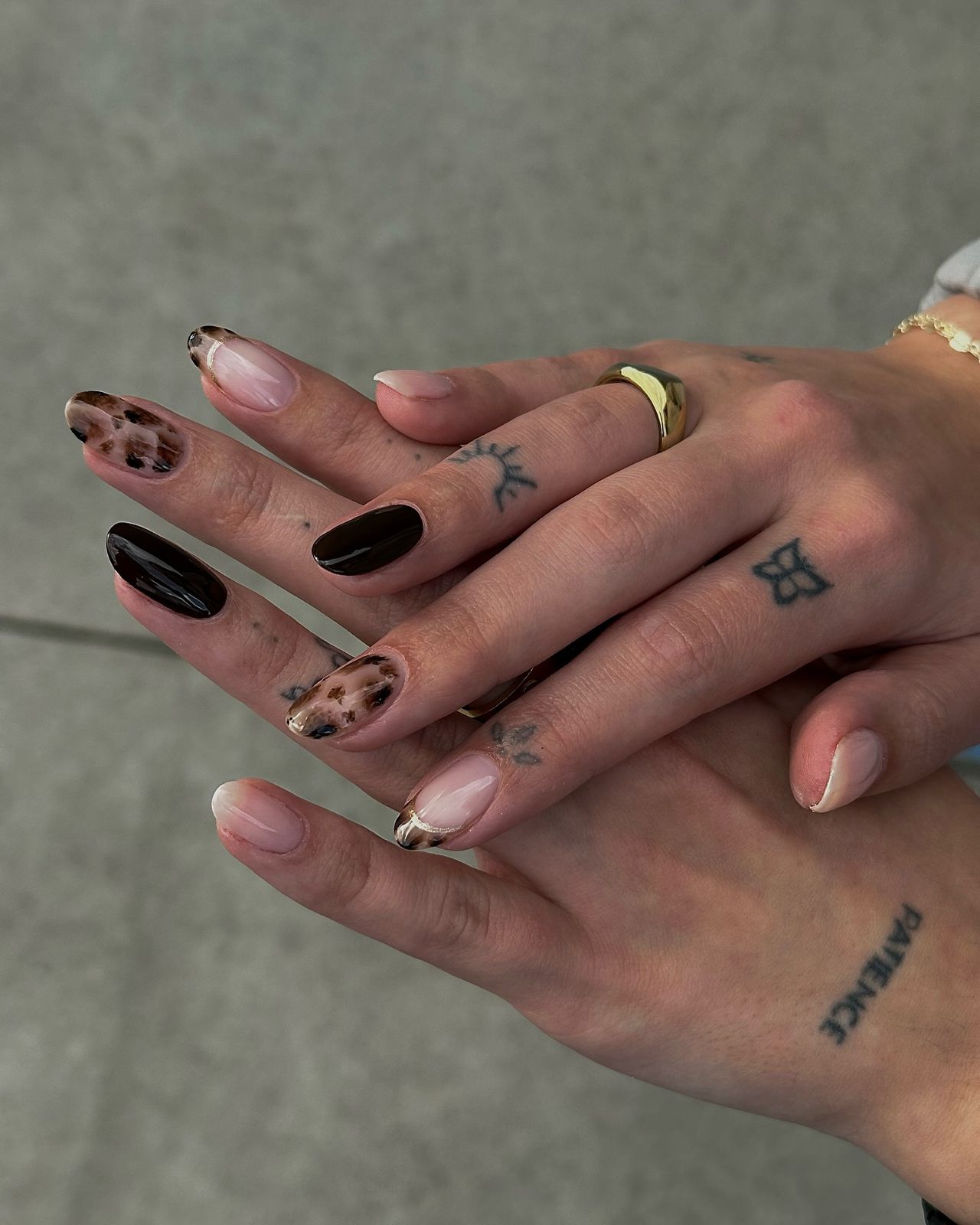 Two hands with manicured nails, one with black polish and leopard spots, the other nude with gold accents.

