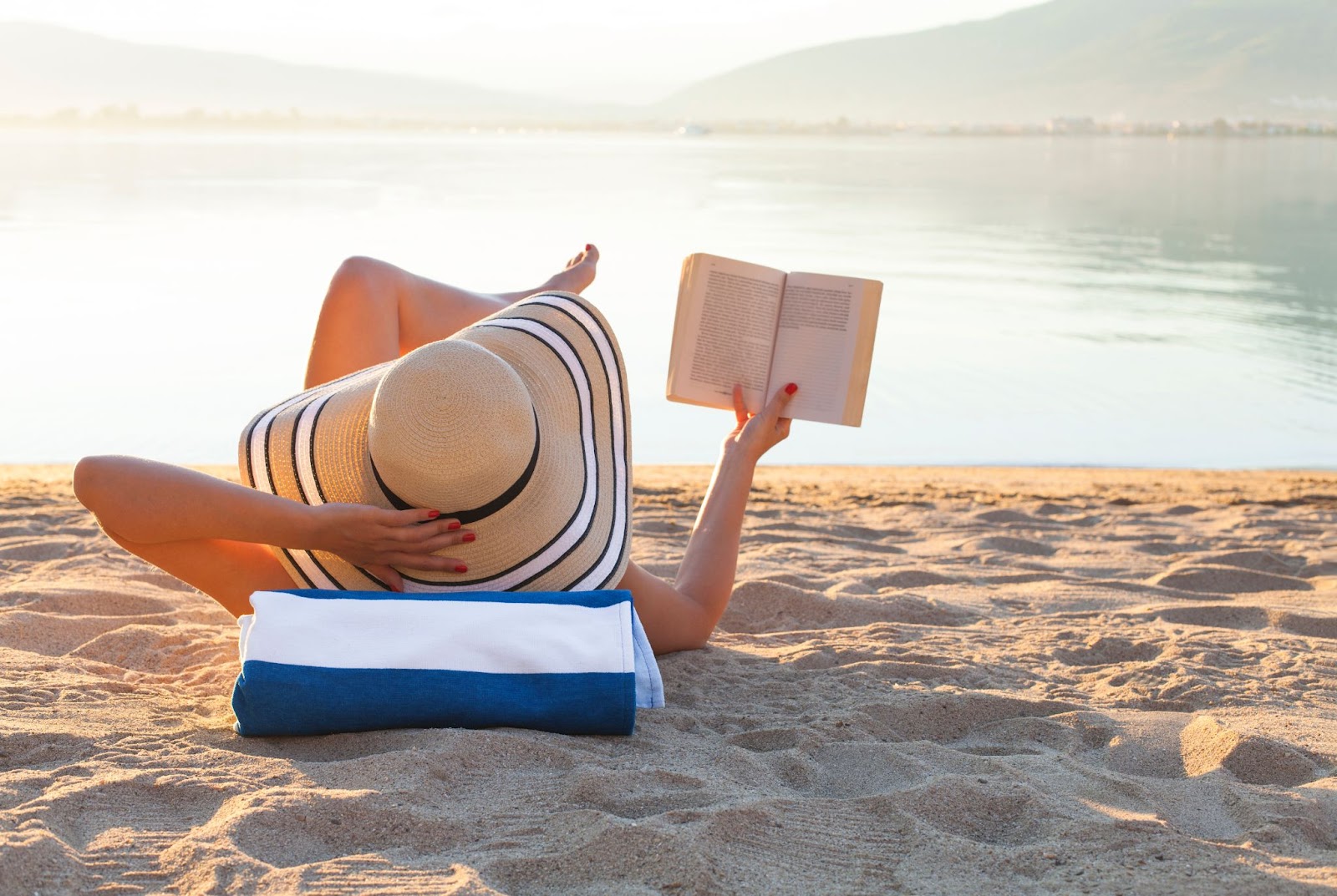 Woman laying out on the sand reading a book