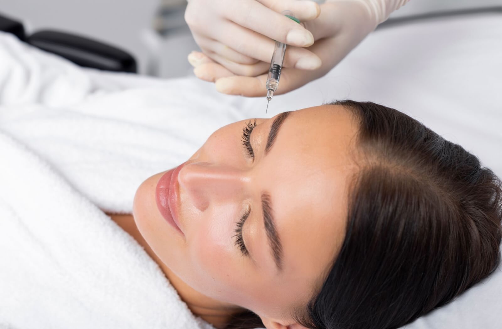  Person receiving a Botox injection near the eyebrows, demonstrating a non-surgical treatment option for hooded eyelids