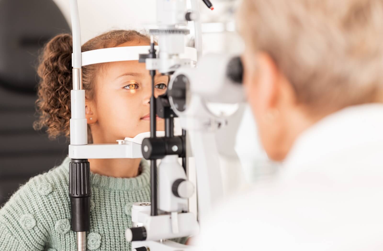 An optometrist examines a child's eye using a slit lamp.