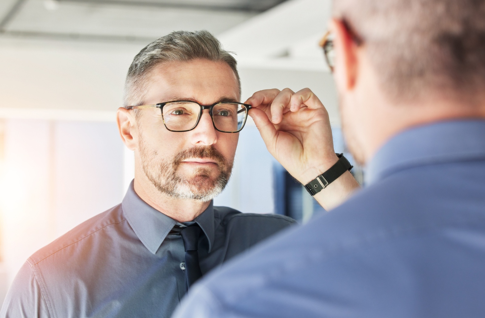 A man admires his new glasses in the optometrist's office.