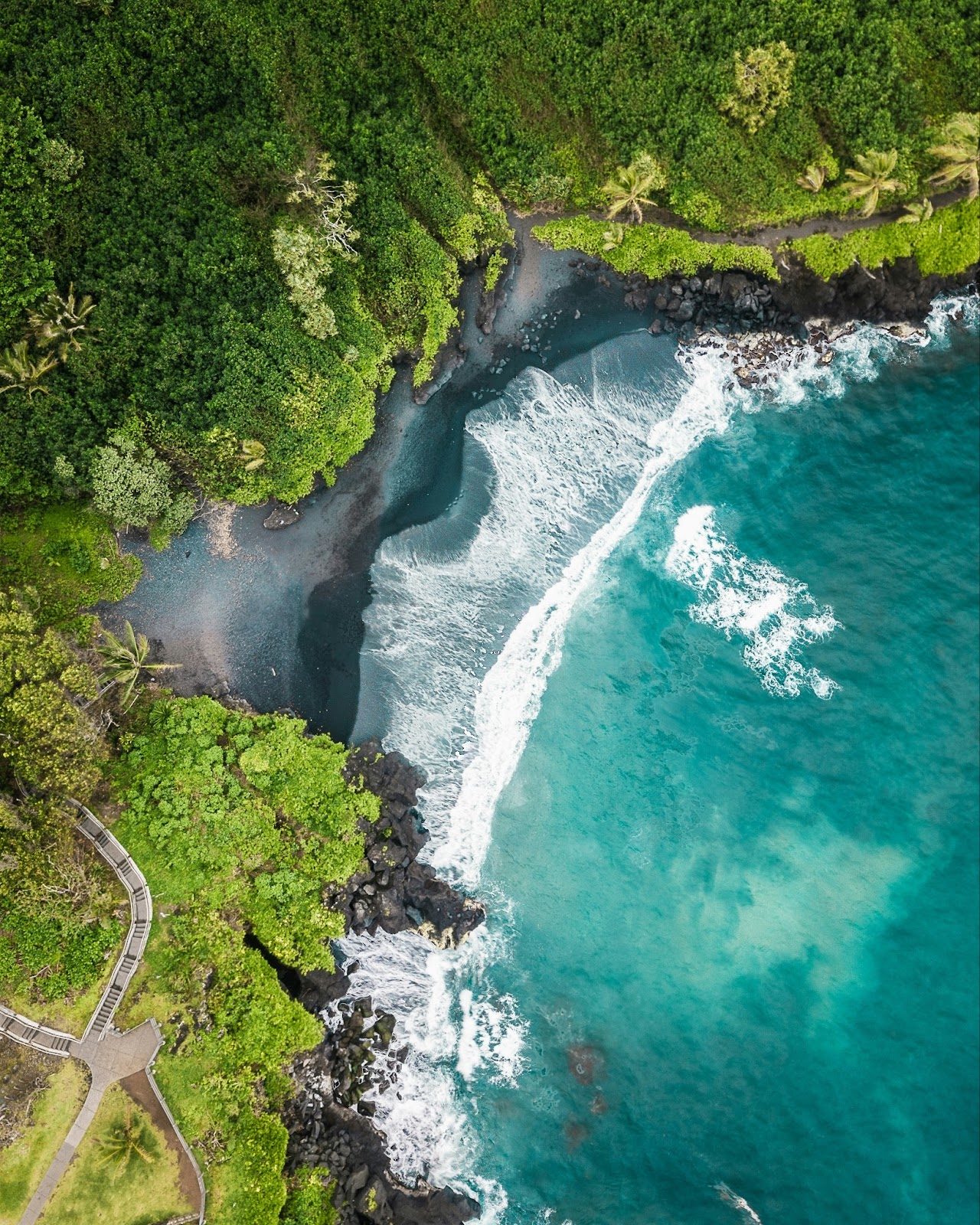 A winding coastal road with lush greenery, black sand beaches, and waterfalls, capturing the beauty of the Road to Hāna.