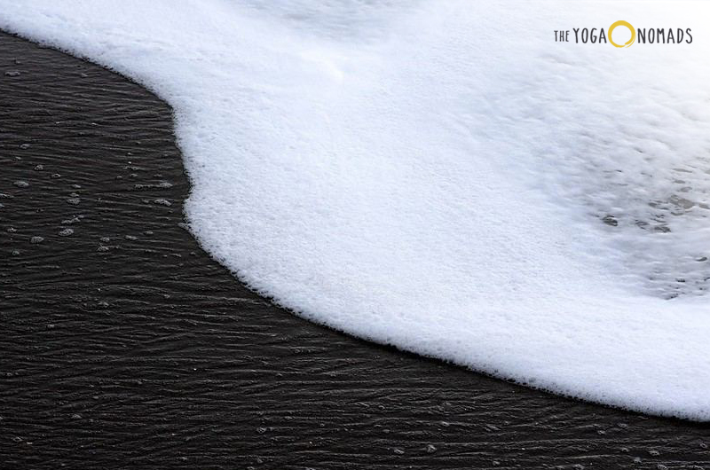 Is yin good or bad? The image shows a close-up of a dark textured surface with white foam on one side, which appears to be water with foam formed on it. The contrast between the dark water and the white foam creates an interesting texture and pattern.