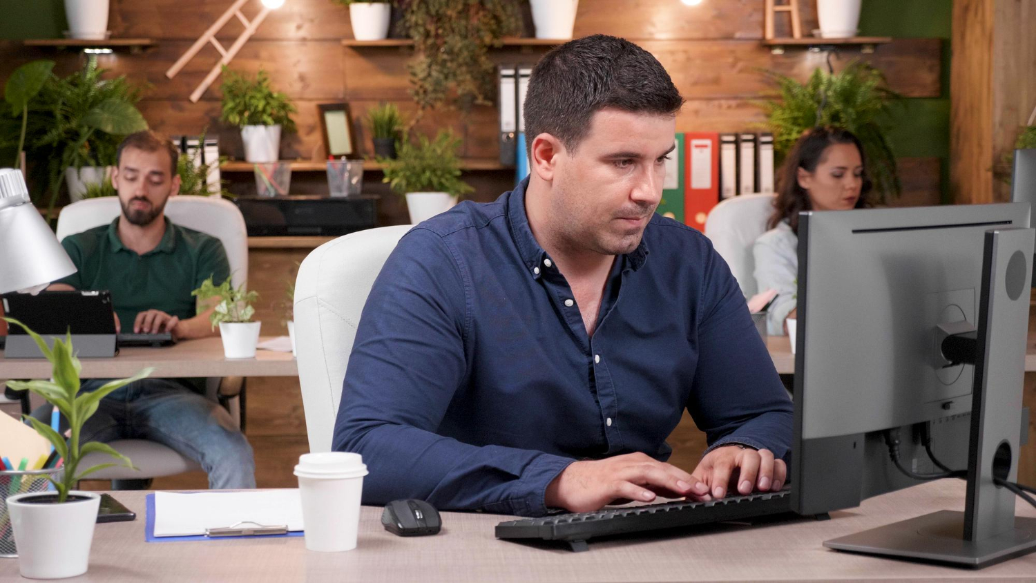 A very tall man works uncomfortably at a small desk, highlighting why a personalized ergonomics assessment for office workers is important.