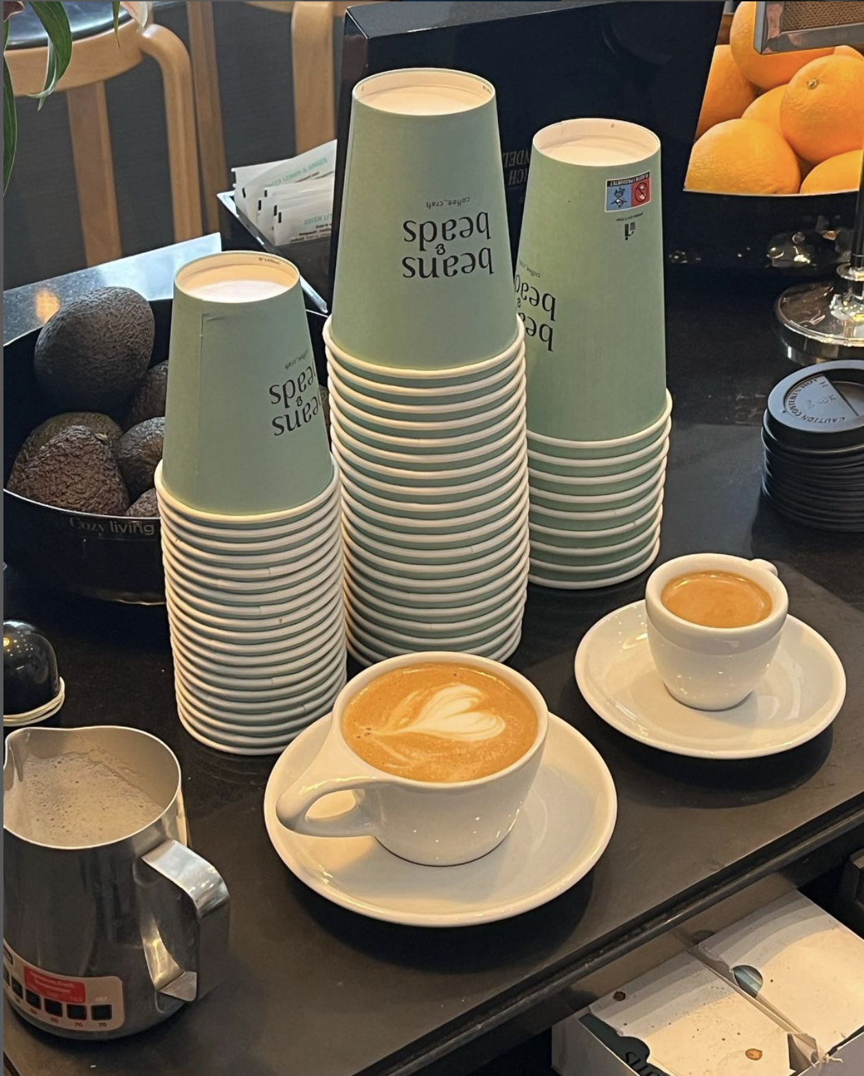 A coffee shop counter displaying stacks of light green branded takeaway cups.