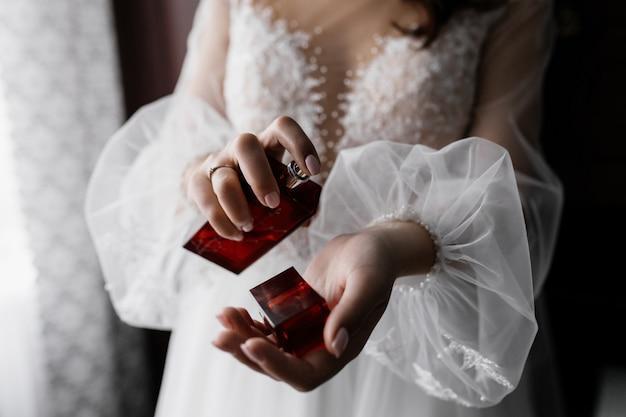 Fiancee in white fashionable dress with beautiful sleeves and perfume in hands