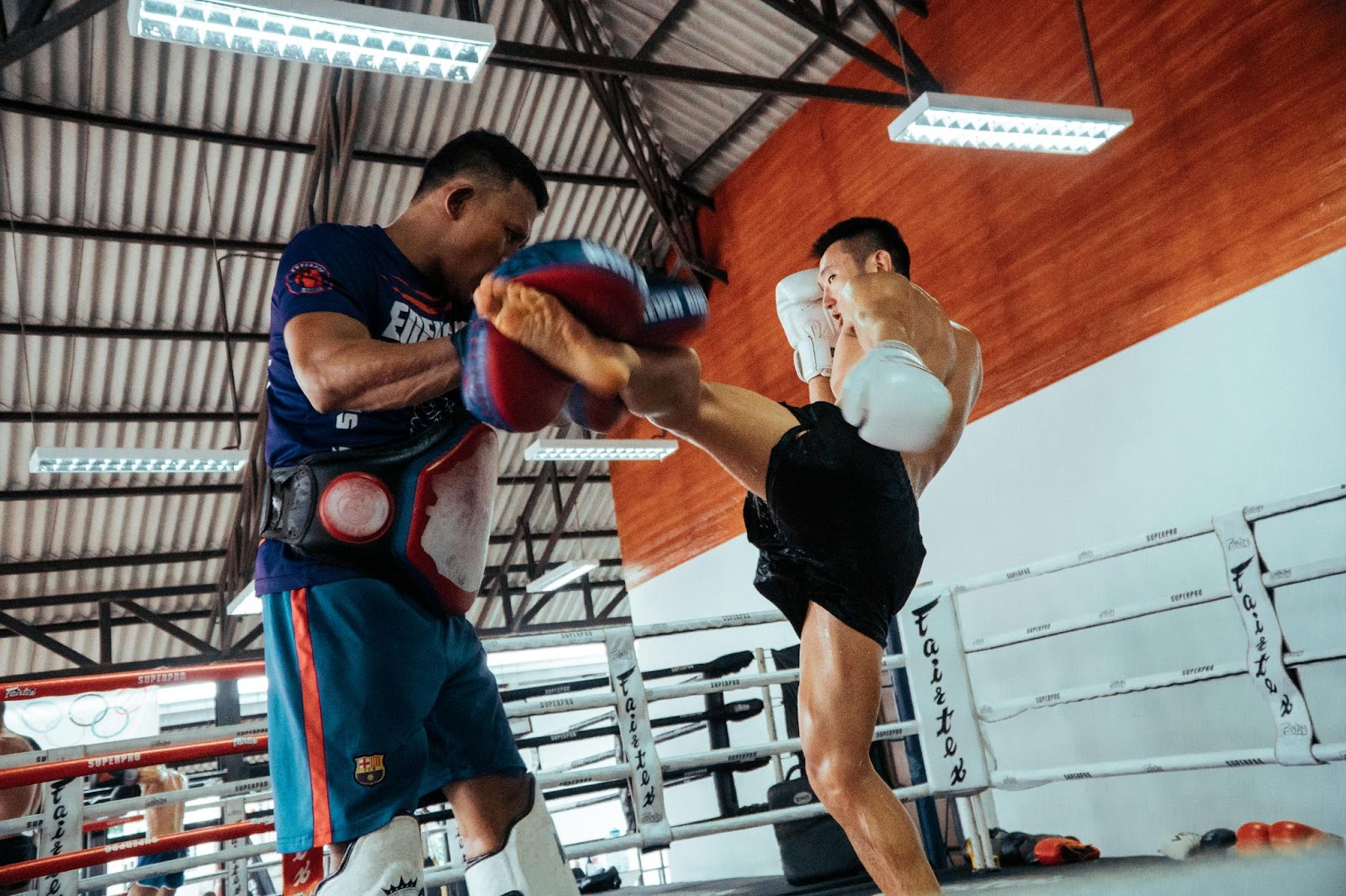 A taekwondo student practicing kicks with an instructor in the ring