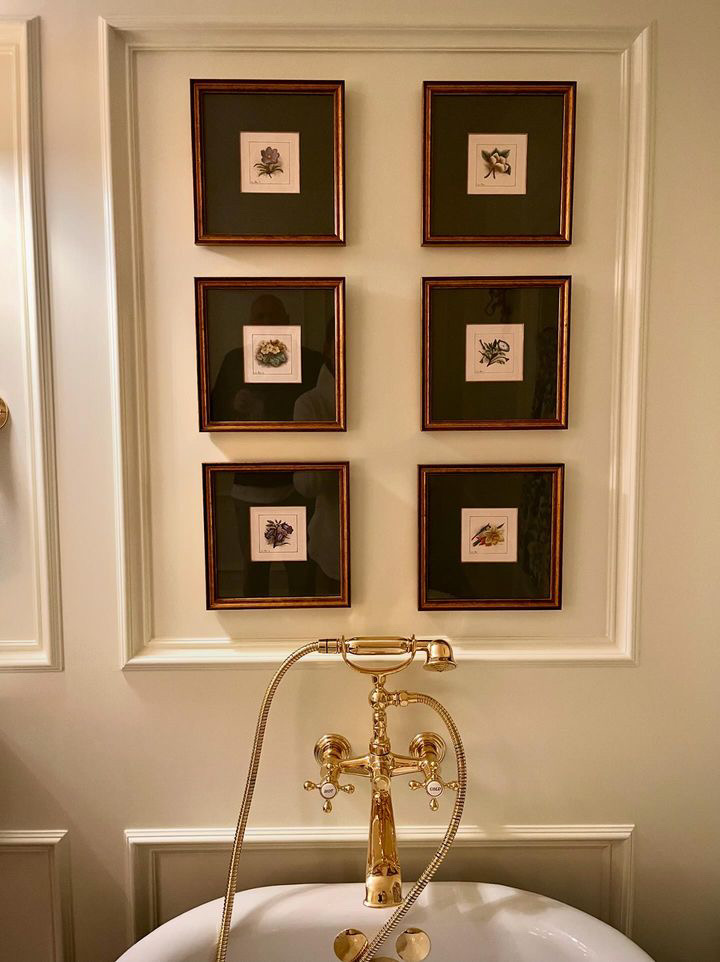 A brass tub faucet below a symmetrical arrangement of six framed botanical prints