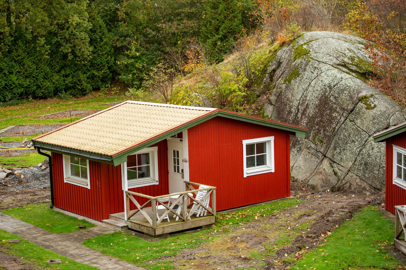 A vibrant red shome surrounded by lush greenery, featuring a large boulder and towering trees, showcasing a unique blend of modern architecture and natural landscape.