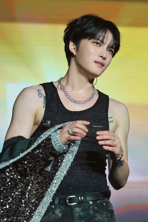 This contain Kim Jaejoong with black hair and piercings on his head is holding a handbag