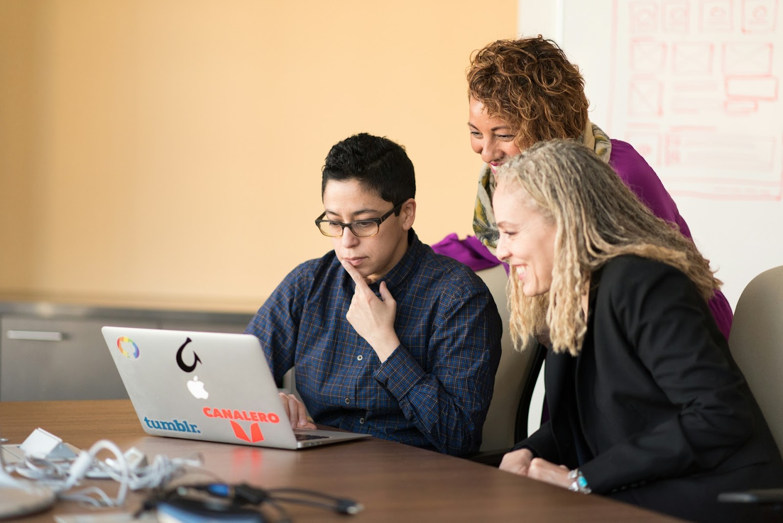 Three women gathered around a table, engaged with a laptop, sharing ideas and enjoying each other's company.