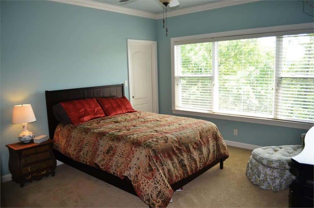 This bedroom has a dark wood bed, a tufted chaise lounge, and a large window bringing natural light in.