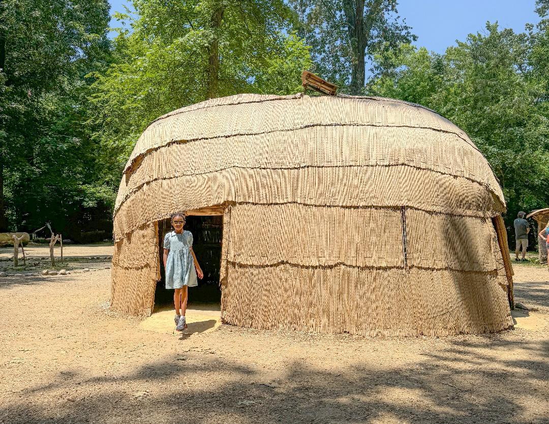 A child standing in front of a straw hut

Description automatically generated